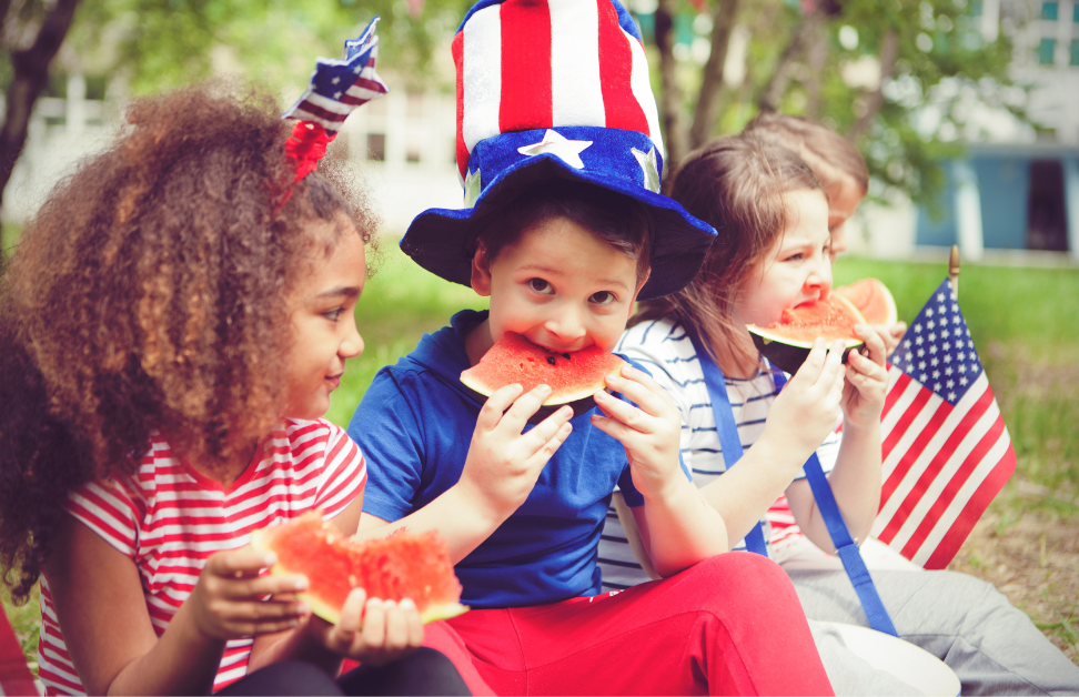 Children enjoy watermelon on July 4th, wearing patriotic attire and holding American flags. Ideal for Southport rentals family gatherings.