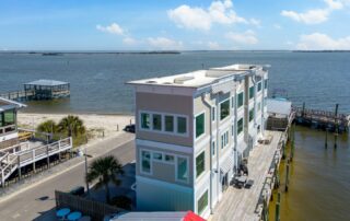 Seaside building with balconies and boardwalk overlooking calm waters, part of Southport rentals, under a clear blue sky.