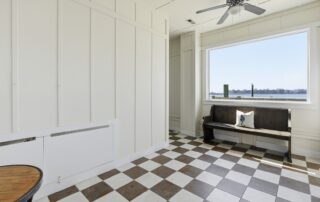 Sunlit room with checkerboard floor, bench, cushion, large window overlooking water. Ideal for Southport rentals.