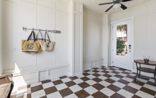 Entryway with checkered floor, wall hooks holding bags, ceiling fan, and door leading outside. Ideal for Southport rentals.