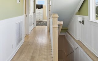 Bright hallway with light wood flooring, green walls, and a wainscoted staircase leading down. View of a room with dresser in Southport rentals.
