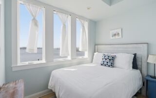 Bright bedroom overlooking water, featuring a white bed with blue pillows, white curtains, and Southport rentals.