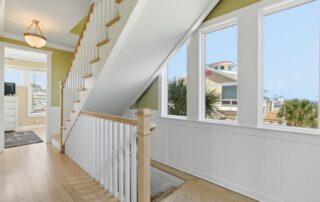 Bright staircase with wooden railings overlooks palm trees and rooftops through large windows, ideal for Southport rentals.