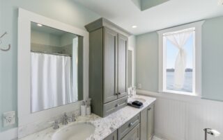 Elegant bathroom with marble-topped double sink, wooden cabinets, and large window with waterfront view. Ideal for Southport rentals.