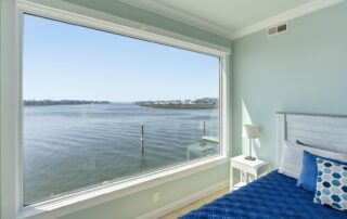 Bedroom with waterfront view, featuring a large window and blue bedding. Ideal for Southport rentals.