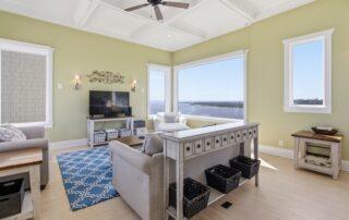 Bright living room with coastal decor, large windows overlooking the ocean, TV, blue rug, and seating area. Ideal for Southport rentals.