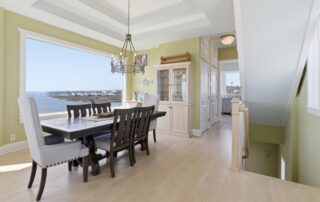 Elegant dining room with ocean view, wooden table, cushioned chairs, chandelier, and pastel green walls; ideal for Southport rentals.