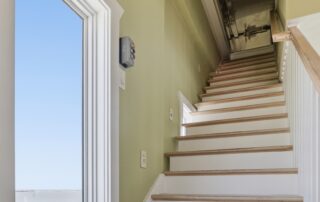 Wooden staircase with green walls, leading to an attic. Bright window view of a calm sea, ideal for Southport rentals.
