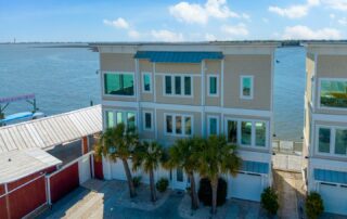 Modern waterfront townhouse with palm trees, offering scenic views of Southport rentals by a calm blue sea under a sunny sky.