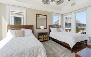 Bright bedroom with two beds, plush white bedding, and a view of nearby buildings through large windows. Ideal for Southport rentals.