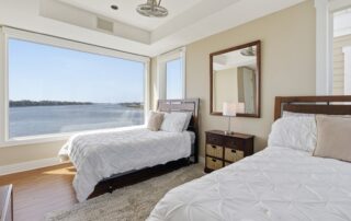 Bright bedroom with two beds, large window with stunning water view, wooden furniture, neutral tones. Ideal for Southport rentals.