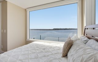 Bedroom with white bedding, large window overlooking a peaceful waterfront, ideal for Southport rentals seeking serene views.