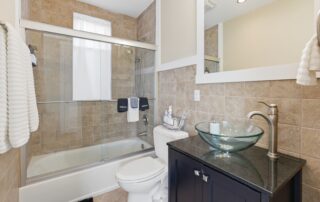 Modern bathroom in Southport rentals, featuring glass vessel sink, sleek faucet, tiled walls, and glass-enclosed shower-tub combo.