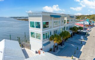 Modern waterfront condos near the marina, Southport rentals, palm trees lining the street, blue sky and calm waters in the background.
