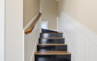 Narrow staircase with wooden steps and white wainscoting, leading to a bright landing, typical of Southport rentals.