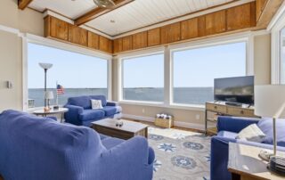 Cozy living room with blue sofas, ocean view windows, TV, and American flag, showcasing a relaxing Southport rentals spot.
