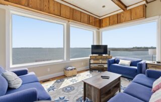 Cozy, nautical-themed living room with blue sofas, large windows offering ocean views, and a TV. Ideal for Southport rentals relaxation.