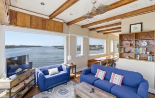 Bright living room with river views, cozy blue sofas, bookshelf, and dining area, ideal for Southport rentals.