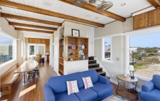Cozy beachside living room with blue sofas, wooden beams, large windows, and scenic view. Southport rentals ideal for relaxation and comfort.