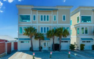 Modern three-story beach house with palm trees, large windows, and garage. Ideal for Southport rentals under clear blue skies.