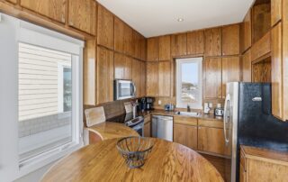 Cozy kitchen with wood cabinets, stainless steel appliances, round table with a fruit basket, window view of Southport rentals by the water.