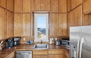 Wood-paneled kitchen with stainless steel appliances, sink, and ocean view. Ideal for Southport rentals.