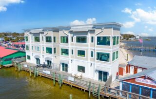 Modern waterfront building in Southport with balconies overlooking the pier, ideal for Southport rentals. Bright, sunny day with clear skies.