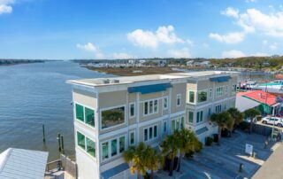 Waterfront building under blue skies near a river, with palm trees lining the front. Ideal for Southport rentals offering scenic views.