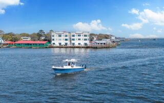 Blue boat sailing by waterfront buildings under a bright sky, showcasing scenic Southport rentals.