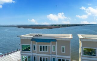 Modern waterfront buildings with large windows overlook a serene lake under a clear blue sky, ideal for Southport rentals.