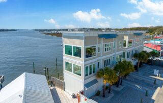 Modern waterfront building beside a river with palm trees, under a blue sky. Perfect for Southport rentals with scenic views.