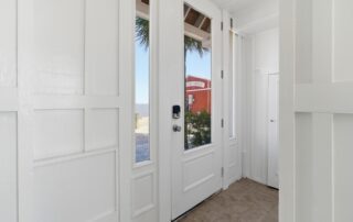 Bright entryway with white walls and tile floor, glass door offering view of red building and beach, ideal for Southport rentals.