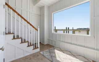 Bright stairway with wooden railings, large window overlooking the water, and sunlight on a textured rug, typical of Southport rentals.