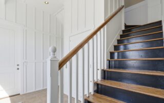White paneled entryway with dark wood stairs and railing, ideal for Southport rentals. Beige tiled floor adds modern touch.